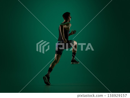 Male runner jumping forward in motion on dark green studio background. 138929157