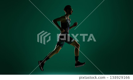 Male runner captured mid stride with steady motion on dark green studio background 138929166