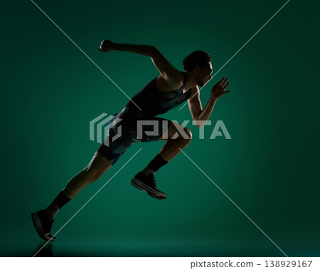Male athlete leaning forward in low sprint pose on dark green background. 138929167