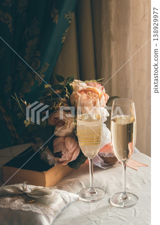 Two glasses of champaign for a broom and a bride. Wedding decor. Glasses with champaign. Bible and pillow with wedding rings. Romantic decor. Wedding anniversary. Love concept. Wedding celebration.  138929977