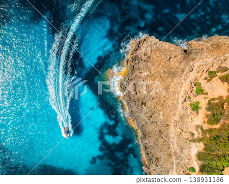Aerial view of motorboat making waves near rocky coastline Aerial view of motorboat making waves near rocky coastline 138931186