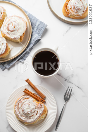 Freshly baked cinnamon rolls with white icing and a cup of black coffee on a light marble background Freshly baked cinnamon rolls with white icing and a cup of black coffee on a light marble background 138931627