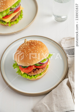 Two beef burgers with tomato, cheese, and lettuce on a plate on a light wooden background Two beef burgers with tomato, cheese, and lettuce on a plate on a light wooden background 138931637