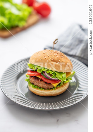Beef burger with tomato, cheese, and lettuce on a plate on a white marble table Beef burger with tomato, cheese, and lettuce on a plate on a white marble table 138931642