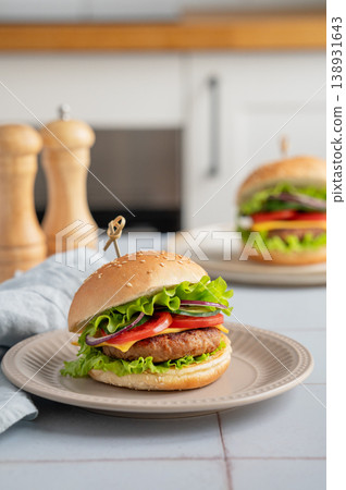 Meat burger with tomato, cheese, and lettuce on a plate on a table with spice and napkin Meat burger with tomato, cheese, and lettuce on a plate on a table with spice and napkin 138931643