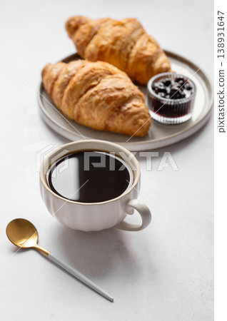 Cup of espresso coffee and fresh croissants on a light background with berry jam and spoon. Cup of espresso coffee and fresh croissants on a light background with berry jam and spoon. 138931647