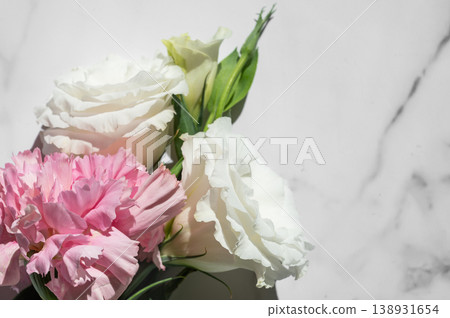 Fresh pink carnations and white eustomas on a marble background with sunlight, top view. Fresh pink carnations and white eustomas on a marble background with sunlight, top view. 138931654
