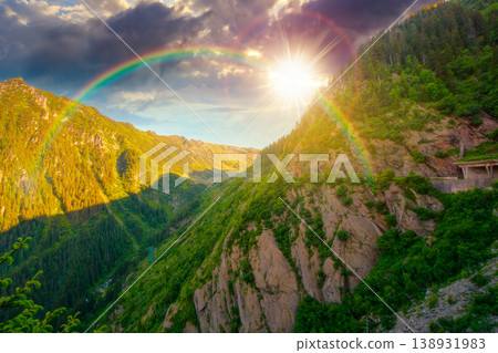 sunset over valley in summer mountains. Gorgeous mountainous landscape. Rocky cliffs and forested slopes under cloudy sky. Scenery of mountain ridge in evening light. sunny weather with rainbow sunset over valley in summer mountains. Gorgeous mountainous landscape. Rocky cliffs and forested slopes under cloudy sky. Scenery of mountain ridge in evening light. sunny weather with rainbow 138931983