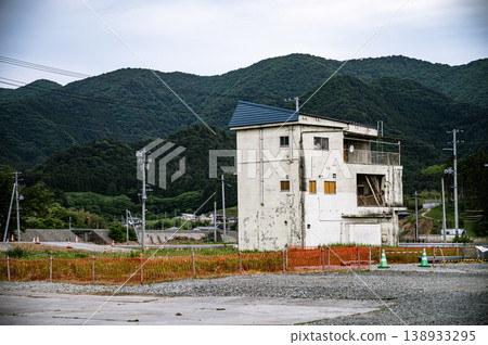 一座破舊的白色建築矗立在空地上，遠處有連綿的山脈。 138933295