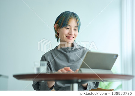 A woman with blonde and blue hair is using a tablet indoors. A woman with blonde and blue hair is using a tablet indoors. 138933780