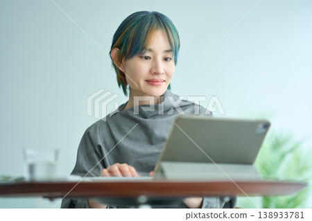 一位有著金色和藍色頭髮的女子正在室內使用平板電腦。 一位有著金色和藍色頭髮的女子正在室內使用平板電腦。 138933781