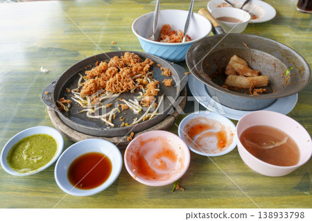 Leftover Thai street food remains on a table. Fried oyster pancake with bean sprouts on a hot plate, glass noodles in a clay pot, and dipping sauces in small bowls. Finished meal at a local eatery. Leftover Thai street food remains on a table. Fried oyster pancake with bean sprouts on a hot plate, glass noodles in a clay pot, and dipping sauces in small bowls. Finished meal at a local eatery. 138933798