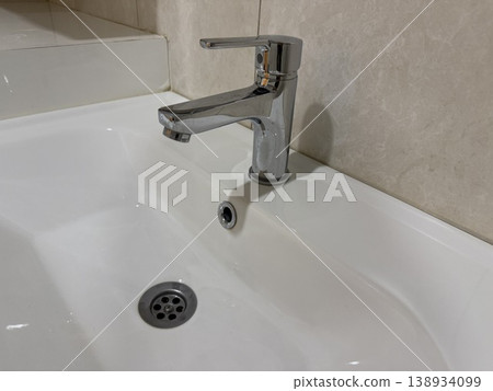 Chrome faucet over white sink in bathroom setting showing clean and modern design background Chrome faucet over white sink in bathroom setting showing clean and modern design background 138934099