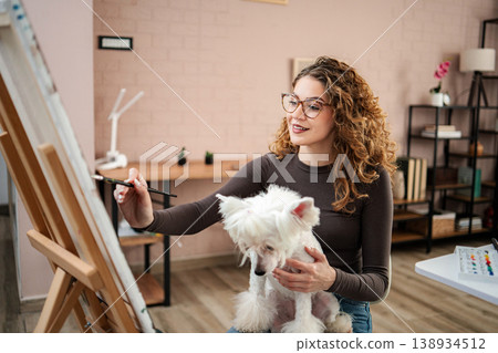 Woman painting while holding her pet dog at home 138934512