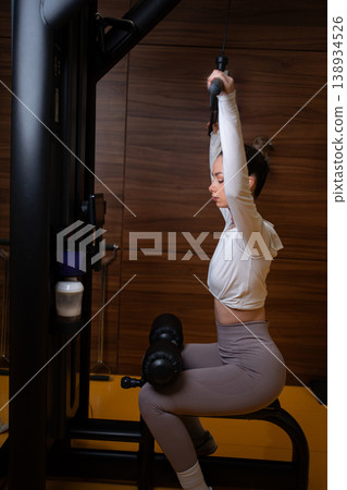 Young adult woman exercising strength training a pulldown machine Young adult woman exercising strength training a pulldown machine 138934526