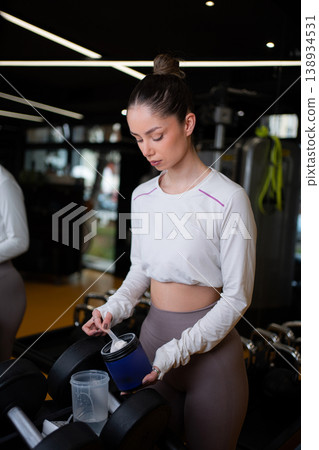 Young adult woman preparing protein powder for workout in gym 138934531
