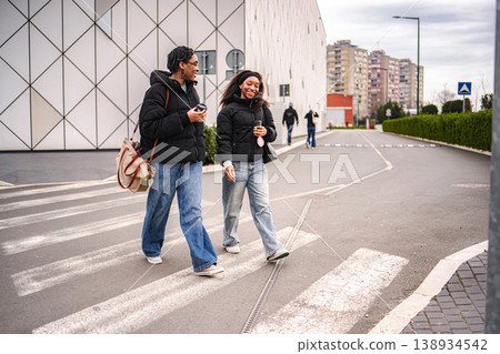 Two young adult women walking and smiling on urban street crossing Two young adult women walking and smiling on urban street crossing 138934542