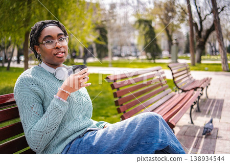 Young adult woman relaxing on park bench drinking coffee 138934544