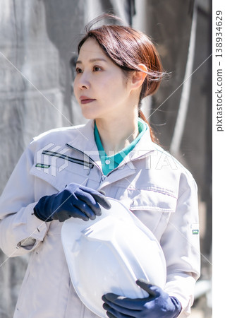 一位身穿工作服、手持安全帽的微笑女工在建築工地上。建築業員工合影。 一位身穿工作服、手持安全帽的微笑女工在建築工地上。建築業員工合影。 138934629