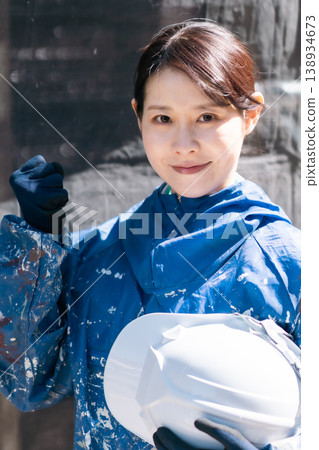 一位面帶微笑的女油漆工,手持安全帽。建築油漆、維護、技術工人、現場女性、戶外。 一位面帶微笑的女油漆工,手持安全帽。建築油漆、維護、技術工人、現場女性、戶外。 138934673