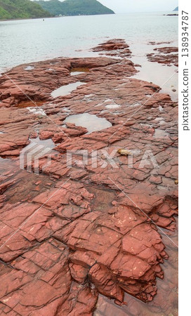 Layered deep red sedimentary rock formations with fractures and water pools in the seaside which is a remote coastal spots in Hung Shek Mun (Red Stone Gate), Plover Cove Country Park, Hong Kong Layered deep red sedimentary rock formations with fractures and water pools in the seaside which is a remote coastal spots in Hung Shek Mun (Red Stone Gate), Plover Cove Country Park, Hong Kong 138934787