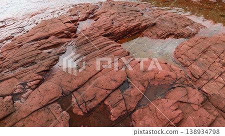Layered deep red sedimentary rock formations with fractures and water pools in the seaside which is a remote coastal spots in Hung Shek Mun (Red Stone Gate), Plover Cove Country Park, Hong Kong 138934798