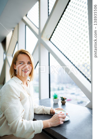 Woman smiling while enjoying coffee in modern cafe Woman smiling while enjoying coffee in modern cafe 138935506