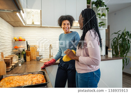 Female friends standing in kitchen baking pizza and talking 138935913