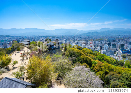 A panoramic view of Matsuyama city from the main citadel plaza of Matsuyama Castle, showcasing lush greenery and skyscrapers. 138935974