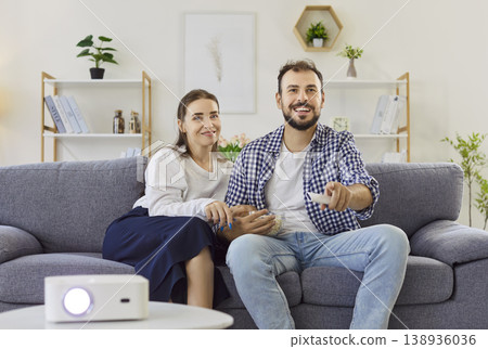 Happy couple watching movie with home projector on sofa in cozy living room Happy couple watching movie with home projector on sofa in cozy living room 138936036