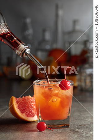 Strong alcohol is poured into a glass with ice and grapefruit juice. 138936046