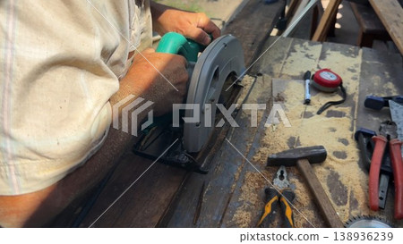 Arms of professional repairman sawing wooden construction with a circular saw at construction. Male hands of adult craftsman cuts wood using electric grind wheel at the site. Slow motion 138936239