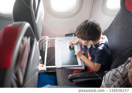Young Boy Engaged in Creative Drawing on Tablet While Traveling in Airplane Young Boy Engaged in Creative Drawing on Tablet While Traveling in Airplane 138936257