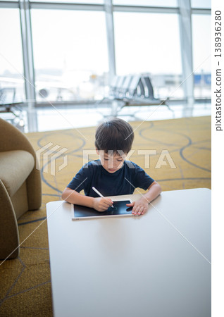 Young Boy Engaged with Tablet in Modern Airport Lounge Setting Young Boy Engaged with Tablet in Modern Airport Lounge Setting 138936280