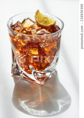 Cocktail with Whiskey, Cola and Lemon Garnish in Crystal Glass on White Wooden Background Cocktail with Whiskey, Cola and Lemon Garnish in Crystal Glass on White Wooden Background 138936300