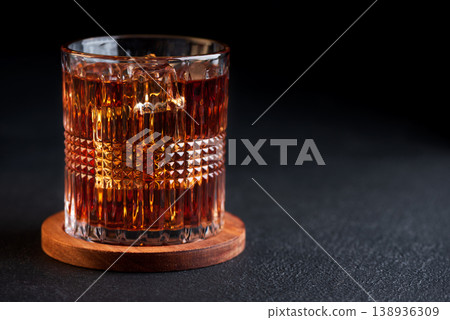 Whiskey Glass with Ice on Wooden Coaster against Dark Concrete Background 138936309