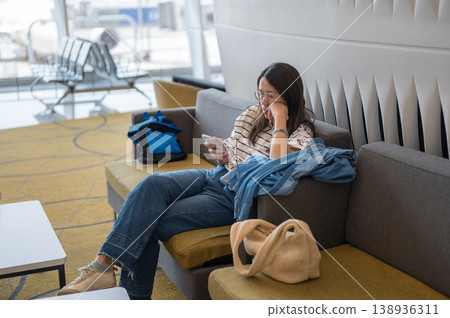 Young Woman Relaxing in Airport Lounge, Using Smartphone While Waiting for Flight Young Woman Relaxing in Airport Lounge, Using Smartphone While Waiting for Flight 138936311