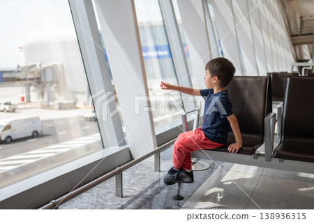 Young Boy Sitting in Airport Lounge Pointing Out of Window 138936315