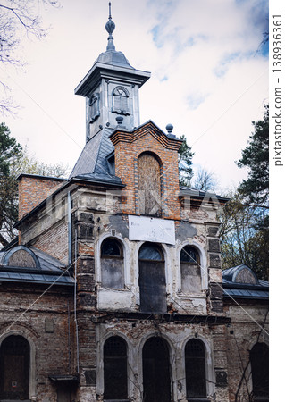 Old brick building with ornate tower and arched windows stands abandoned among trees. Historic property investment, fixer-upper mansion renovation, abandoned estate for sale. Old brick building with ornate tower and arched windows stands abandoned among trees. Historic property investment, fixer-upper mansion renovation, abandoned estate for sale. 138936361