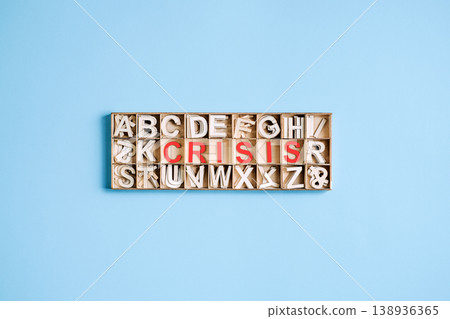 Wooden alphabet box on blue background features red letters spelling word CRISIS. Economic recession risks, global financial instability, stock market crash. 138936365
