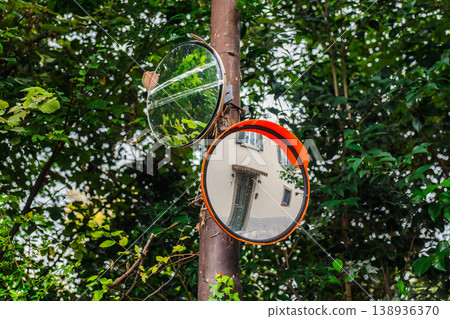 Convex traffic mirrors on pole reflecting house facade among green foliage in Italy Convex traffic mirrors on pole reflecting house facade among green foliage in Italy 138936370