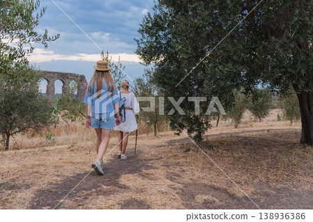Walking mother and teenage daughter in Parco degli Acquedotti Rome near ancient Roman aqueduct ruins at sunset among trees and dry grass Walking mother and teenage daughter in Parco degli Acquedotti Rome near ancient Roman aqueduct ruins at sunset among trees and dry grass 138936386