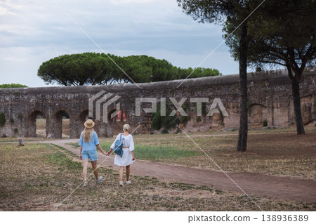 Mother and teenage daughter walking toward ancient Roman aqueduct arches in Parco degli Acquedotti Rome enjoying travel experience in Italy Mother and teenage daughter walking toward ancient Roman aqueduct arches in Parco degli Acquedotti Rome enjoying travel experience in Italy 138936389