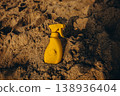 Yellow sunscreen spray bottle partially buried in sand Warm beach scene with textured dunes and summer sun protection concept 138936404