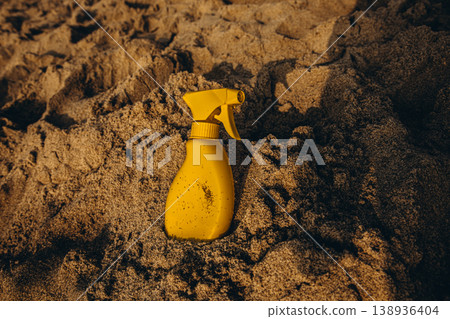 Yellow sunscreen spray bottle partially buried in sand Warm beach scene with textured dunes and summer sun protection concept 138936404