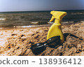 Sunscreen spray bottle placed on sandy shore with sea in background Beach skincare product concept under warm sunlight 138936412