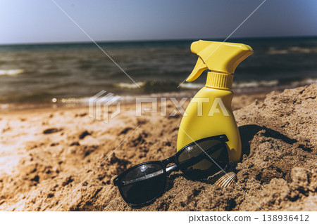 Sunscreen spray bottle placed on sandy shore with sea in background Beach skincare product concept under warm sunlight 138936412