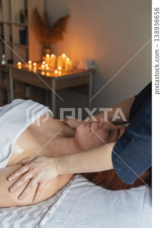 Woman lying on a massage table receiving a professional back and shoulder massage in a relaxing spa environment with candles 138936656