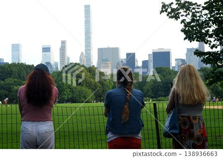 Women Watching Cityscape Peacefully. Three Females Gaze Over Park Fence At Skyline Peacefully Women Watching Cityscape Peacefully. Three Females Gaze Over Park Fence At Skyline Peacefully 138936663