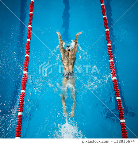 Top view of tattooed male swimmer performing butterfly stroke in pool lane with strong splash. Concept of fitness, strength, endurance, training, discipline and competitive swimming performance 138936674